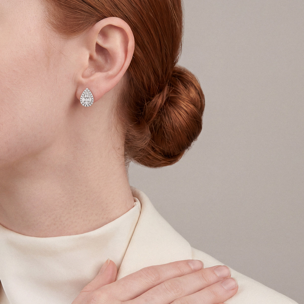 Woman in a cream wool blazer and high mock neck wearing a pear-shaped natural diamond cluster halo stud earring in 14K white gold