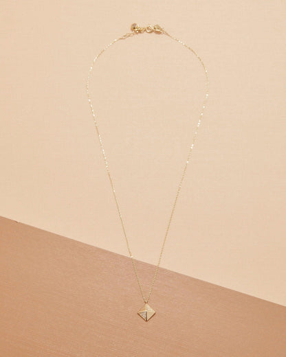 The 14K solid gold pyramid necklace laid flat on a two-tone peach background, showing the full chain and clasp.