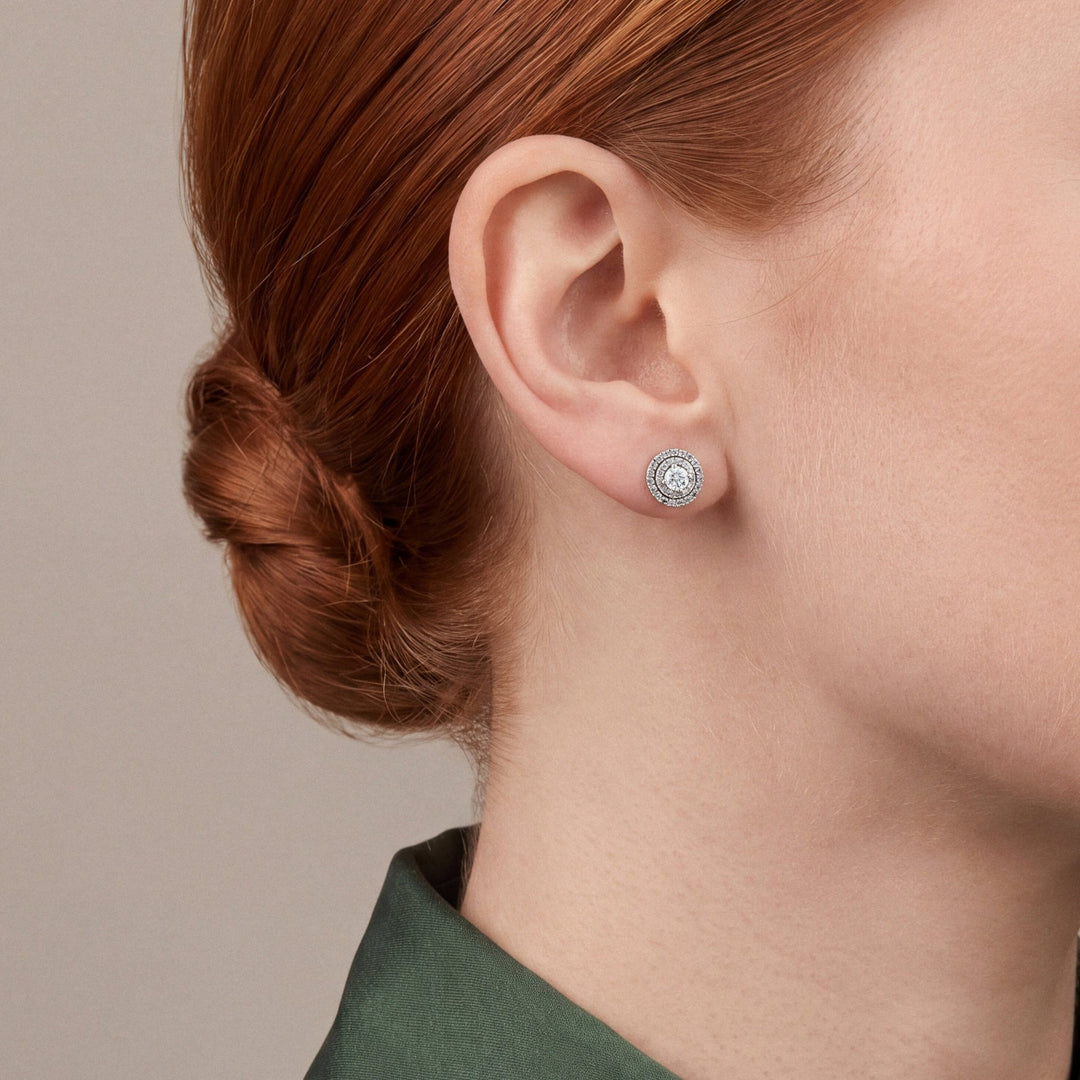 Woman in profile in a forest-green satin shirt with a buttoned stand collar wearing a round natural diamond double halo stud earring in 14K white gold