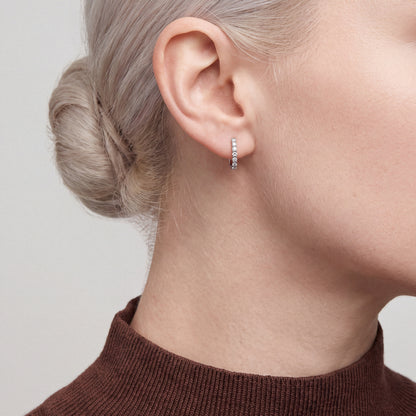 Woman in profile in a chocolate-brown knit mock neck wearing a round natural diamond huggie hoop earring in 14K white gold