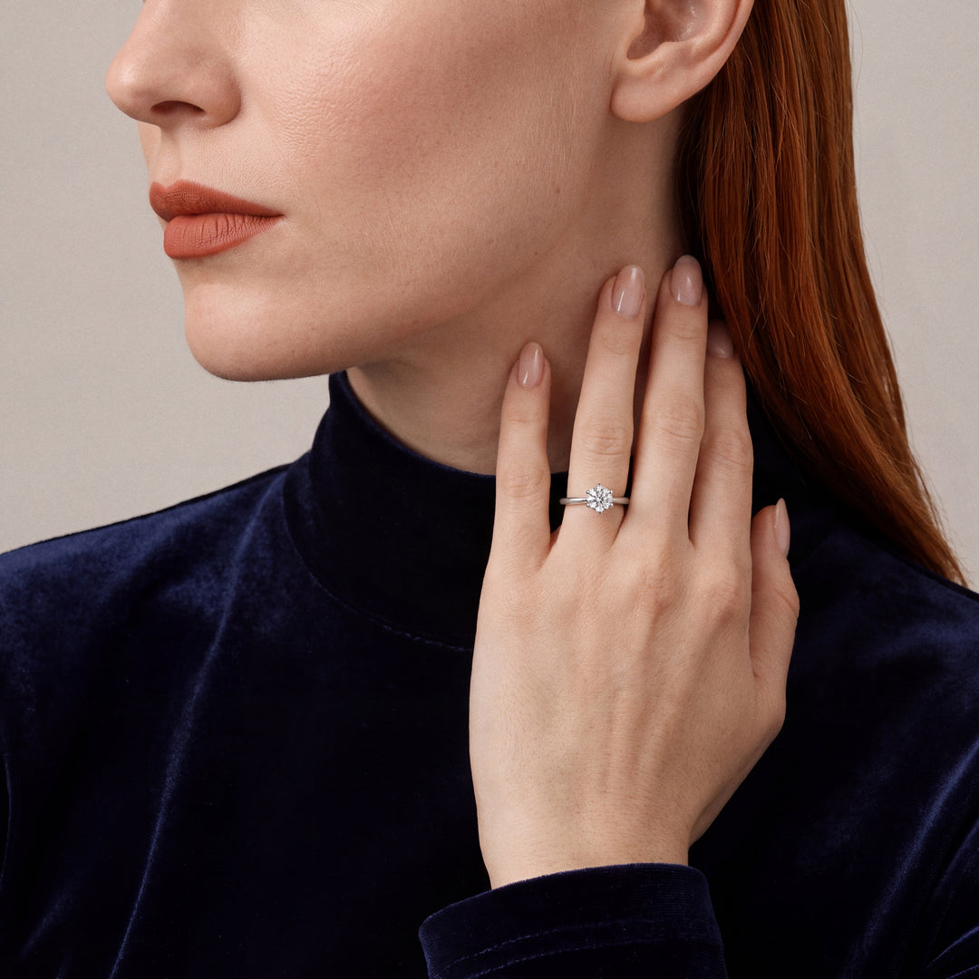 Woman in a midnight-navy velvet mock-neck top wearing a 0.61 ct natural round diamond six-prong solitaire ring in 14K white gold, fingertips at the side of the neck