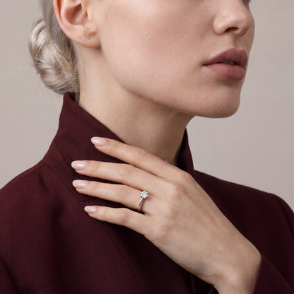 Woman in an oxblood silk-wool stand-collar jacket wearing a 0.61 ct natural round diamond six-prong solitaire ring in 14K white gold on the ring finger, hand at the collar