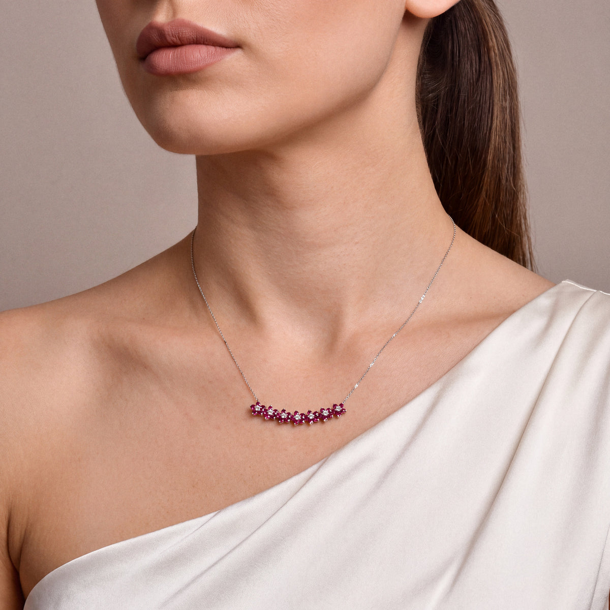 Seven-flower ruby and diamond necklace in 14K white gold on the collarbone, worn with an oyster silk one-shoulder gown