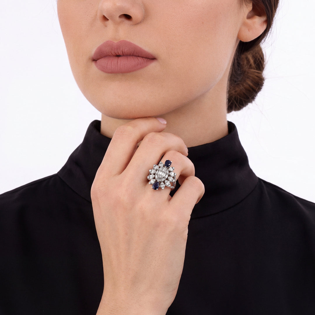 Woman in a black crepe high-neck blouse wearing a sapphire and natural diamond starburst cocktail ring in 14K white gold on the ring finger, fingers curled at the chin