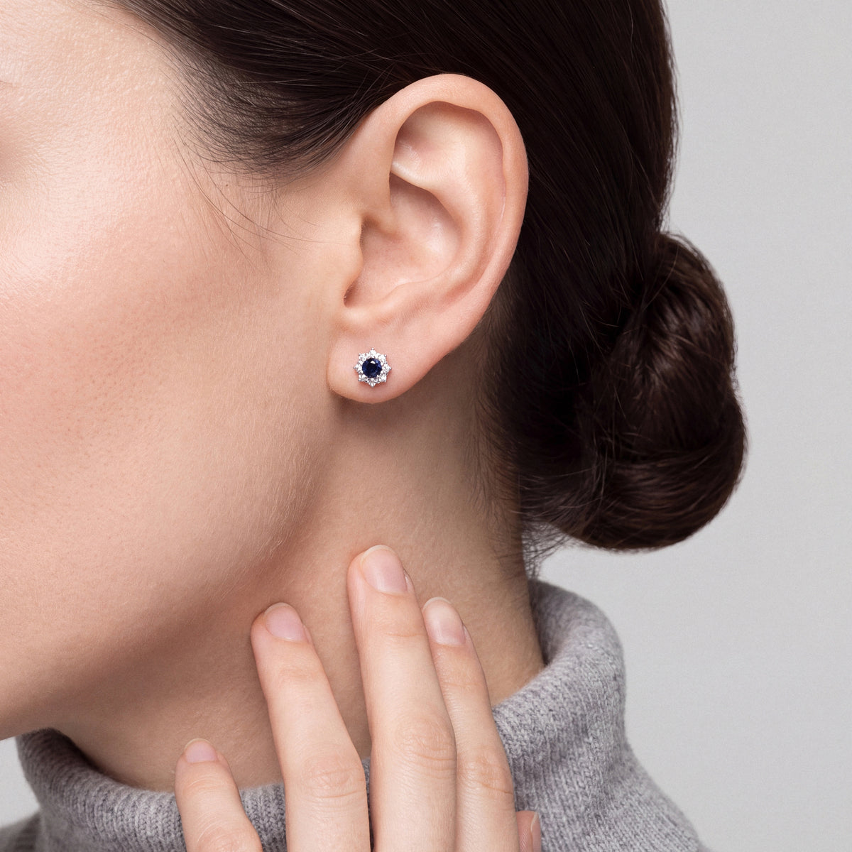 Sapphire and natural diamond halo stud earring in 18K white gold, worn with a grey cashmere high neck