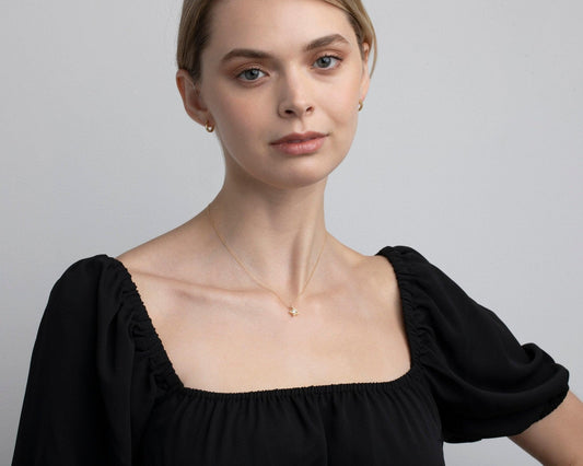 Model wearing the 14K solid gold star necklace with a black square-neck top.