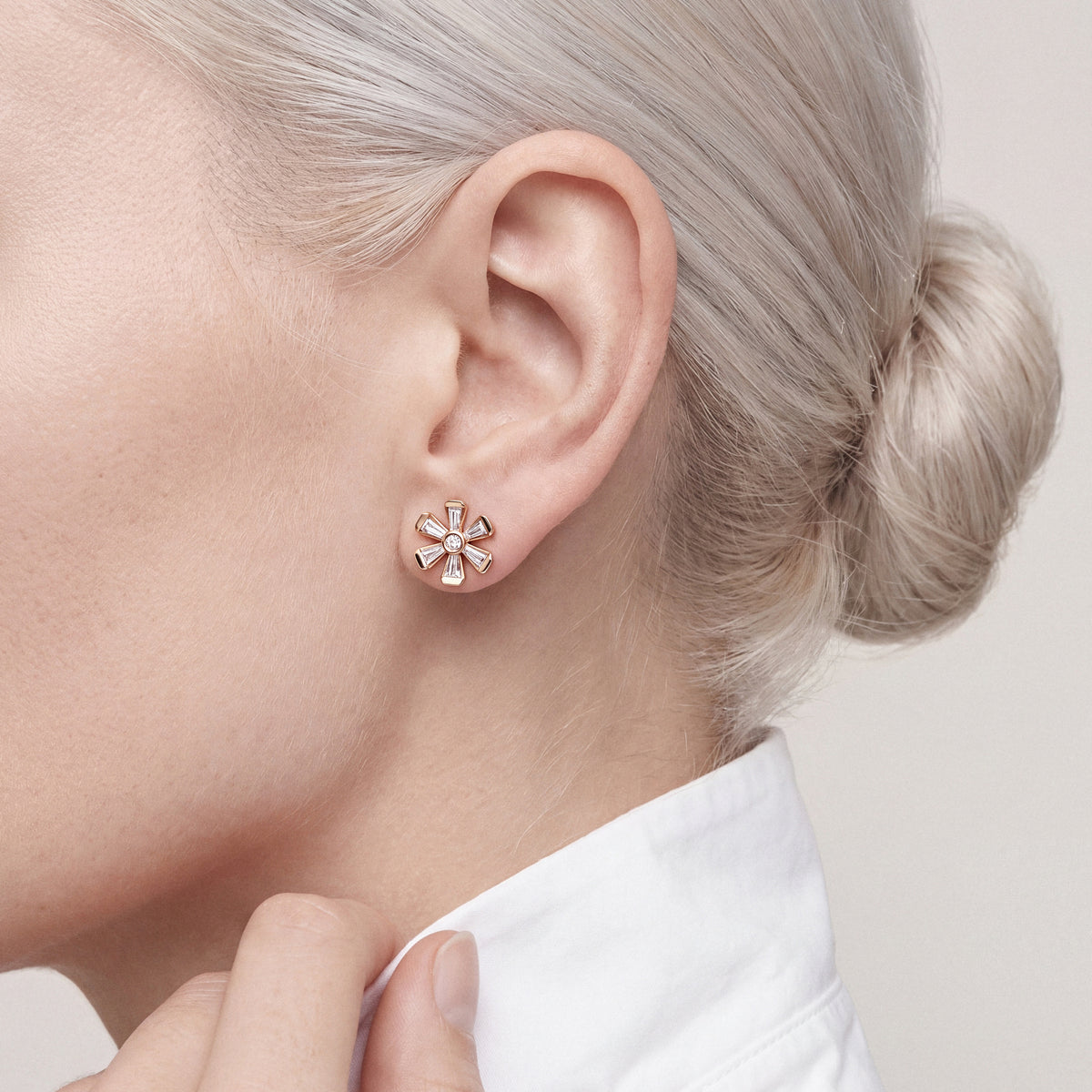 Woman in a white poplin shirt with a turned-up collar wearing a tapered baguette natural diamond flower stud earring in 18K rose gold