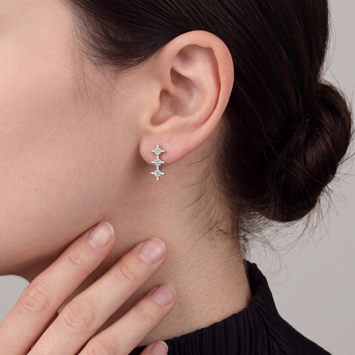 Woman in a black pleated high-neck top wearing a three-star natural diamond drop stud earring in 14K white gold