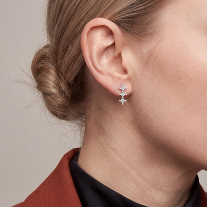 Woman in a rust blazer over a black mock neck wearing a three-star natural diamond drop stud earring in 14K white gold