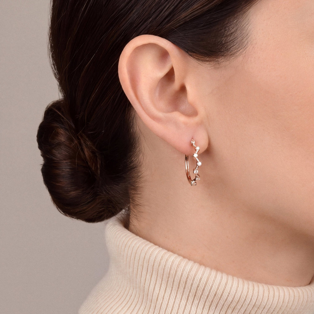 Woman in a cream cashmere turtleneck wearing a natural diamond zigzag hoop earring in 14K rose gold