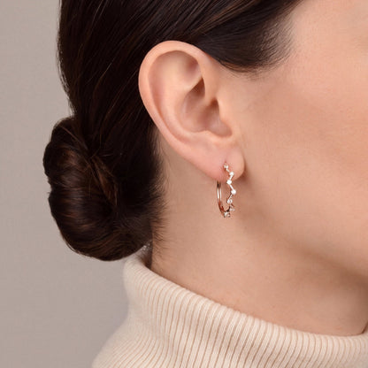 Woman in a cream cashmere turtleneck wearing a natural diamond zigzag hoop earring in 14K rose gold